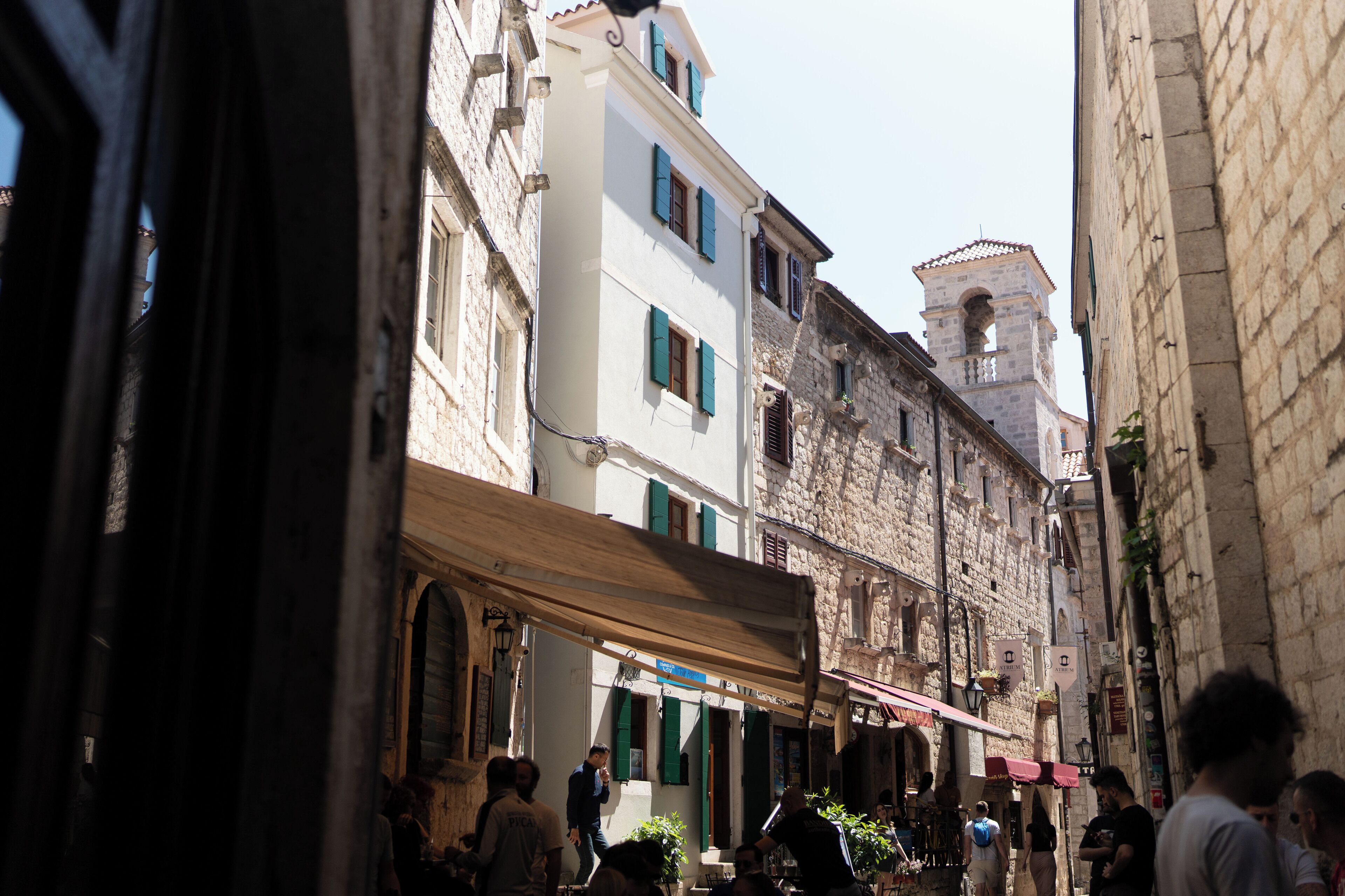 A narrow street with buildings, a bell tower, and people walking.