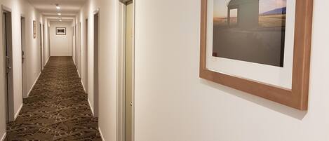 Ein Hotelgang mit Teppichmuster, weißen Wänden und gerahmten Bildern an der Wand.