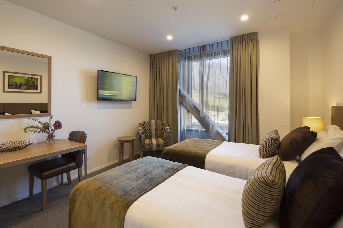 A hotel room with two beds, a desk, a chair, a TV, and a window with curtains.