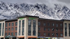 Un hotel con letrero de jardín, varias ventanas y vistas a montañas nevadas.