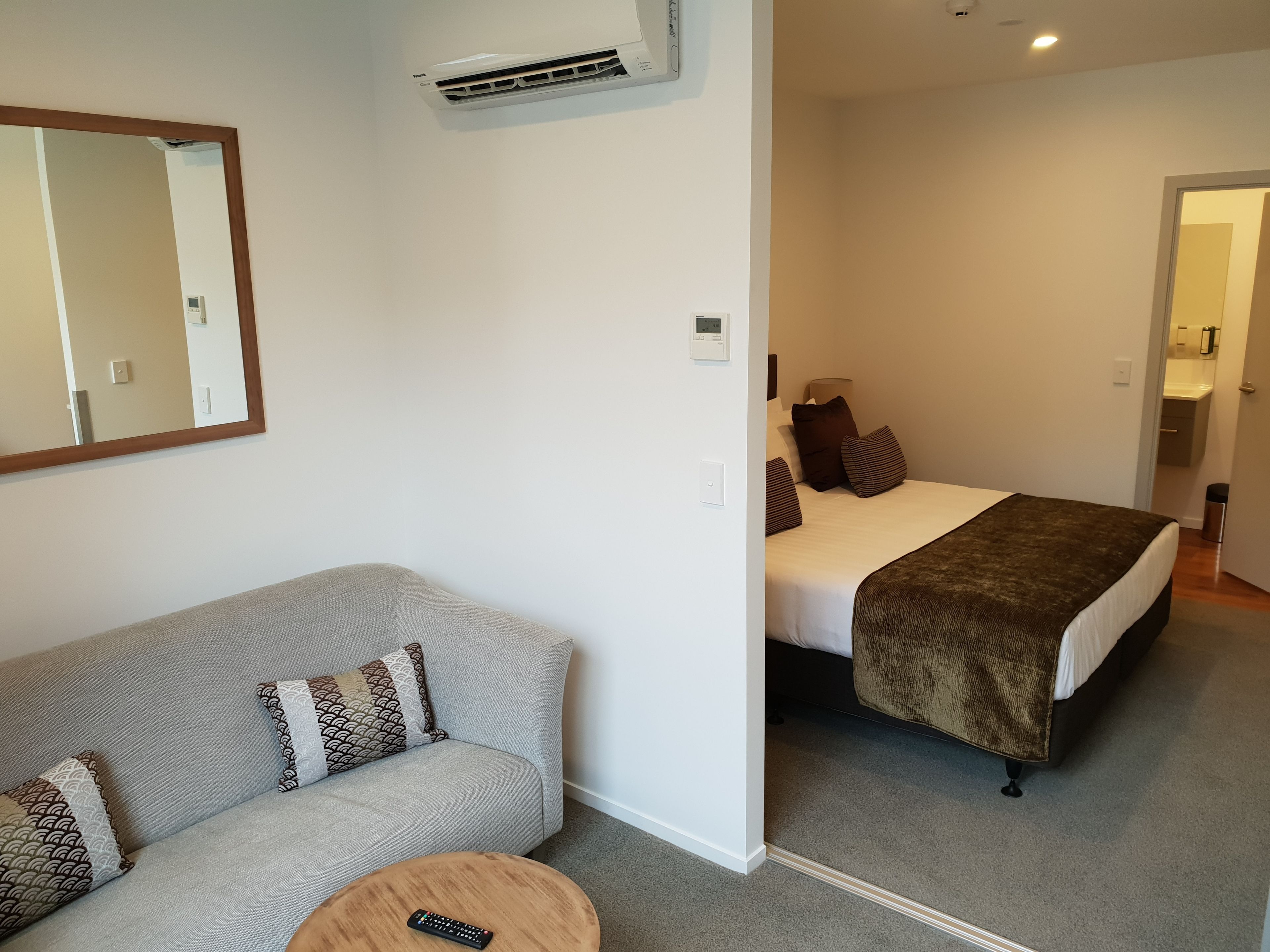 Ein Hotelzimmer mit grauem Sofa, einem Bett mit brauner Decke und einer Klimaanlage an der Wand.