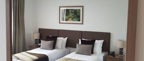 A hotel room with two beds, a nightstand with a phone, a lamp, and a framed picture on the wall.