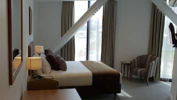 A hotel room with a bed, a desk, a chair, a lamp, and a window with curtains.