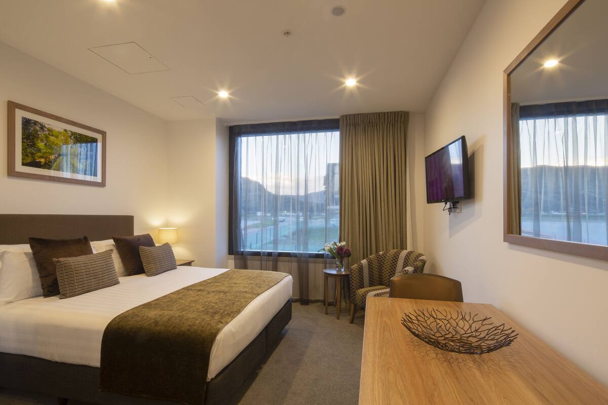 A hotel room with a large bed, a desk, a chair, a TV, and a window with curtains.
