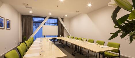 A conference room with a long table, green chairs, and a large window with curtains.