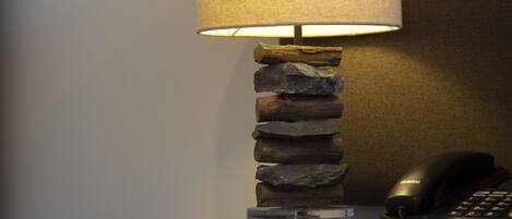 A lamp with a textured shade, a stack of rocks, a glass container, a pen, and a telephone on a table.