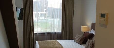 Habitación de hotel con una cama grande, un televisor montado en la pared, una ventana con cortinas y un termostato también en la pared.