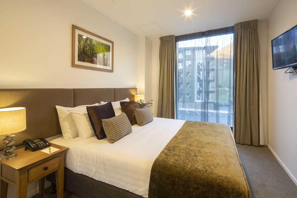 A hotel room with a large bed, a bedside table with a lamp, a telephone, and a framed picture on the wall.