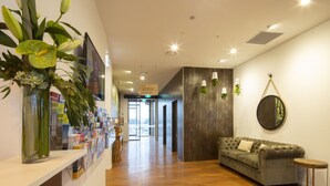 Una moderna zona de recepción con suelo de madera, un sofá gris, un espejo redondo y un arreglo de plantas.