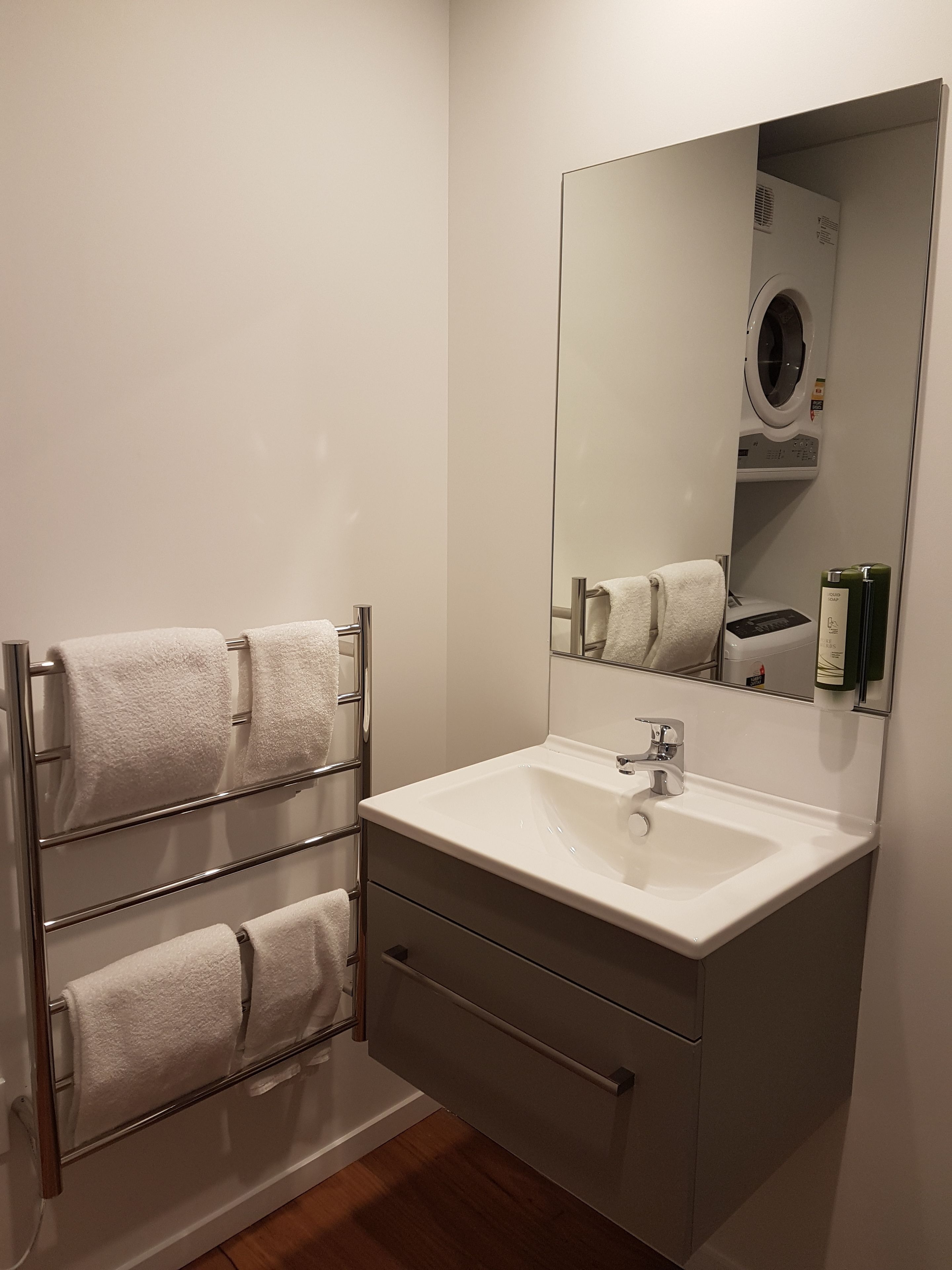 Un bagno moderno con un lavandino bianco, uno specchio e un portasciugamani con diversi asciugamani.
