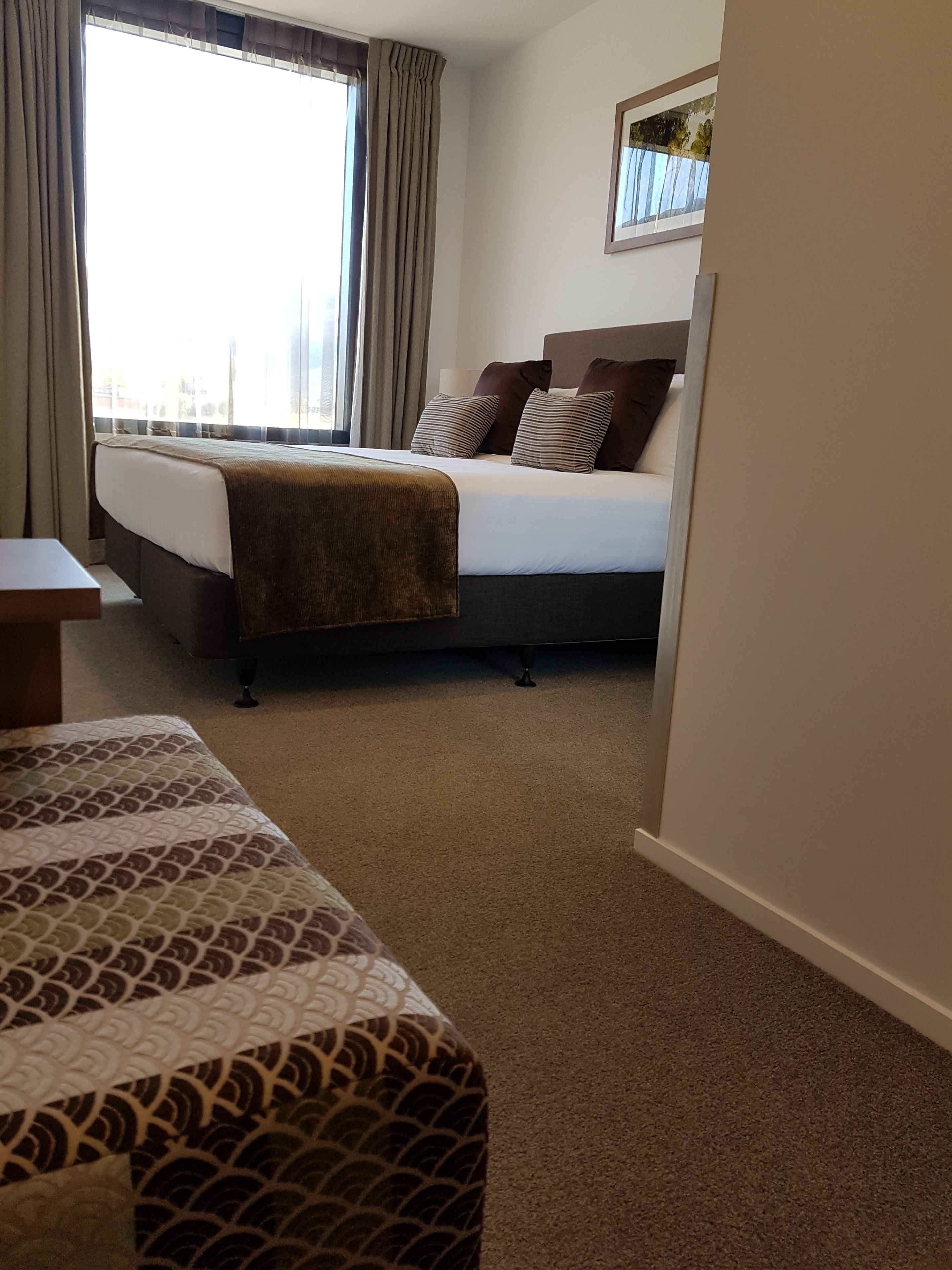 A hotel room with a bed, a bedside table, and a window with curtains.