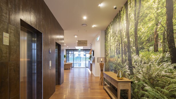 Un vestíbulo de hotel moderno con piso de madera, un ascensor, una recepción y un gran mural de un bosque en la pared.