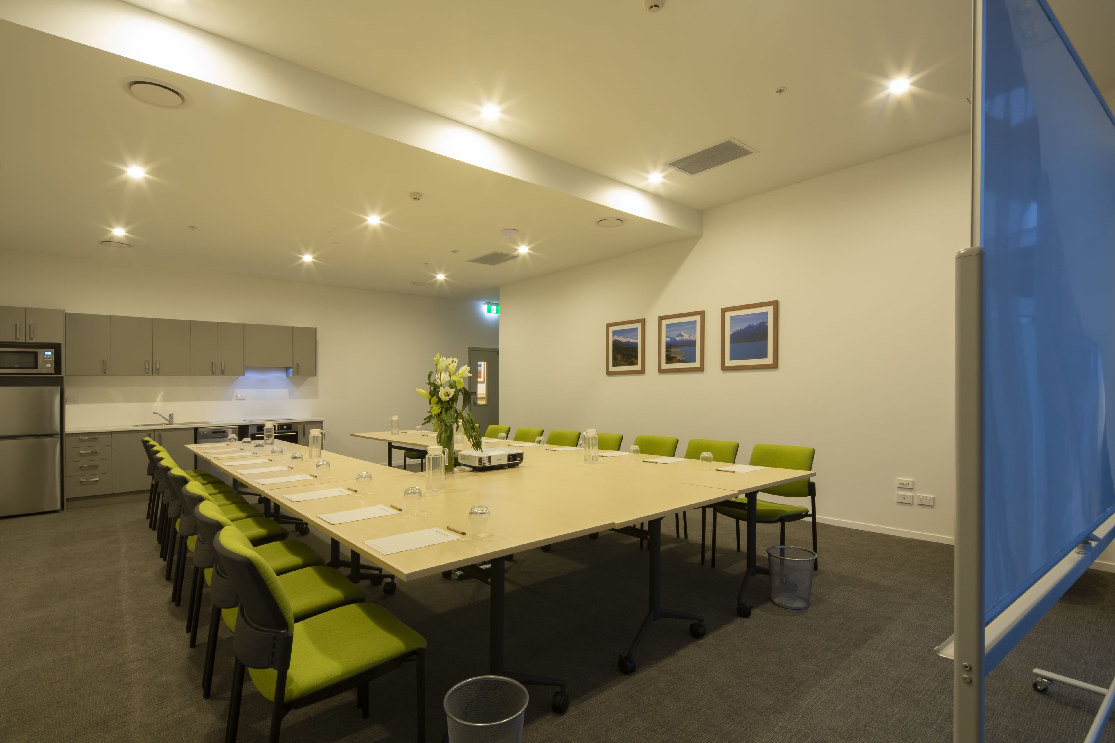 A conference room with a long table, chairs, a projector screen, and a small kitchenette.