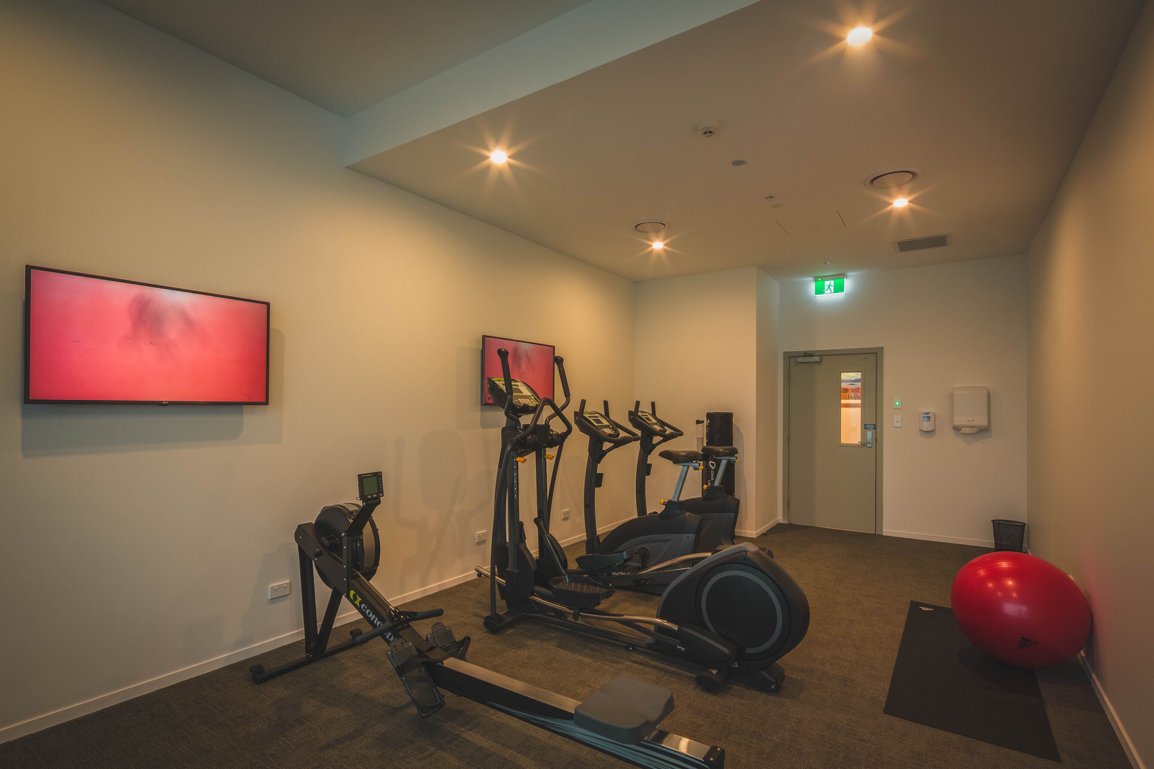 A gym with cardio equipment, a red exercise ball, and a treadmill.