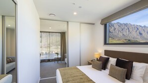 Habitación de hotel con una cama grande, vistas a las montañas, un comedor y una puerta corredera que da a otra habitación.