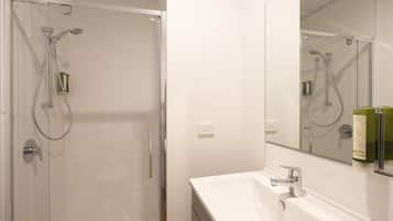 Un baño con cabina de ducha de vidrio, un lavamanos blanco y un espejo sobre el lavamanos.