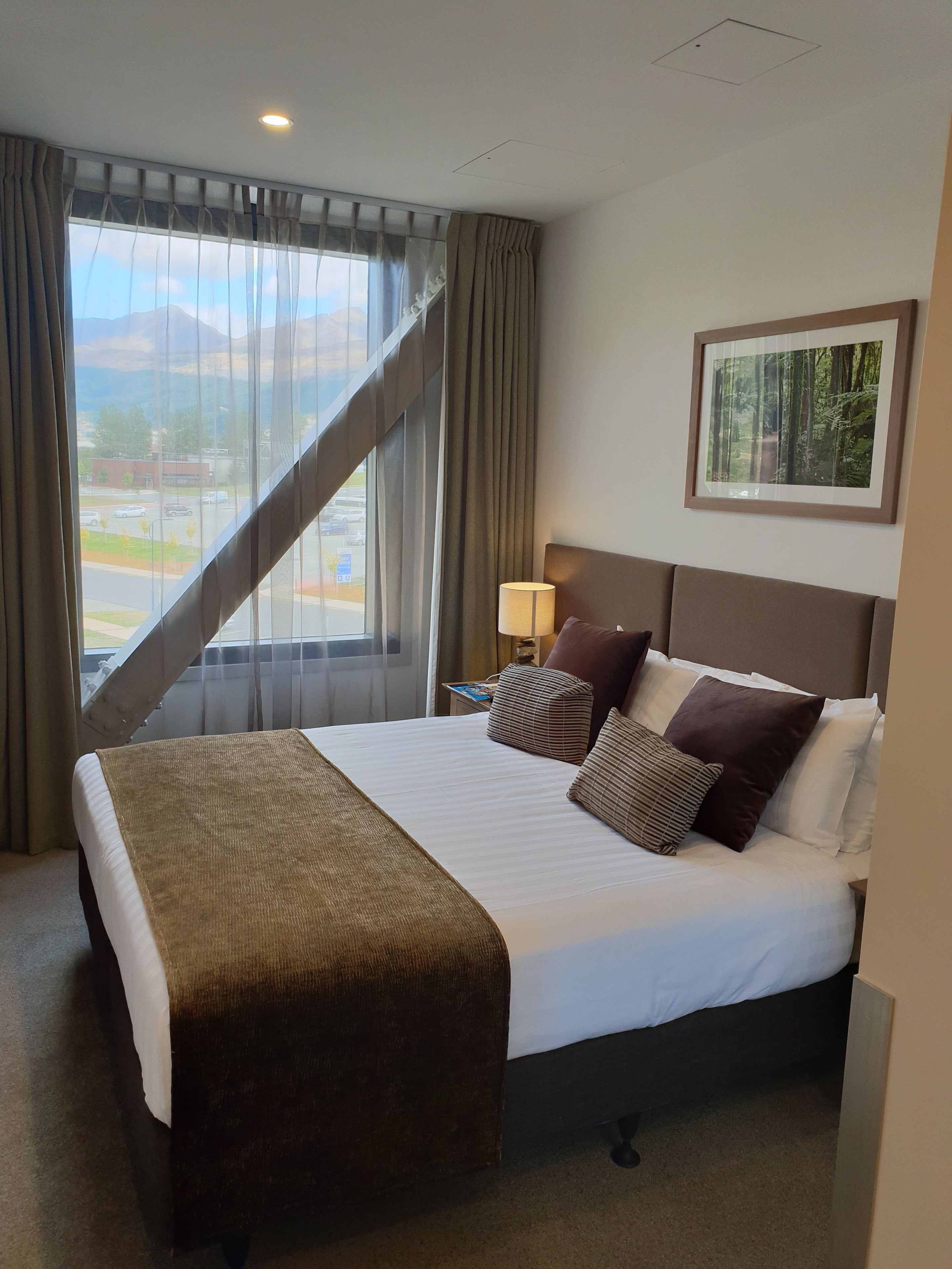A hotel room with a large bed, a nightstand, a lamp, and a window with curtains.