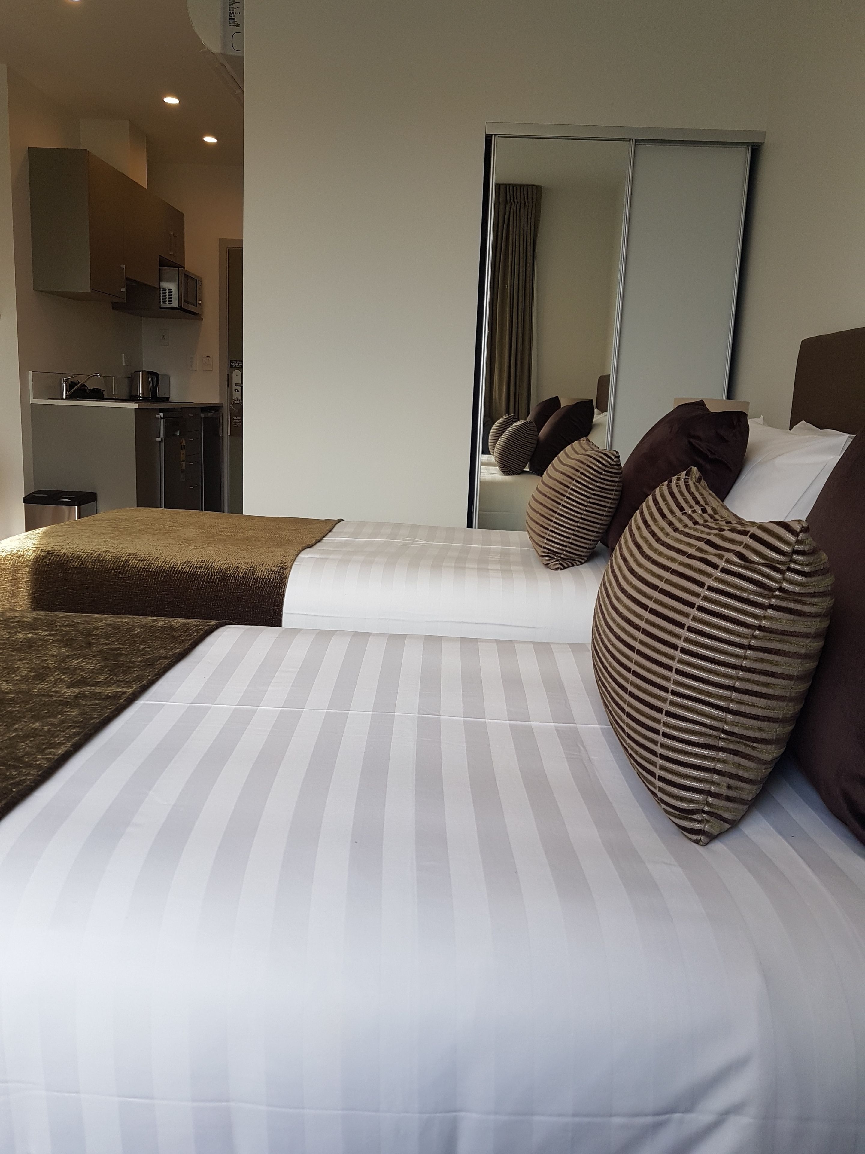 Habitació d'hotel amb un llit, un mirall gran i una cuineta al fons.