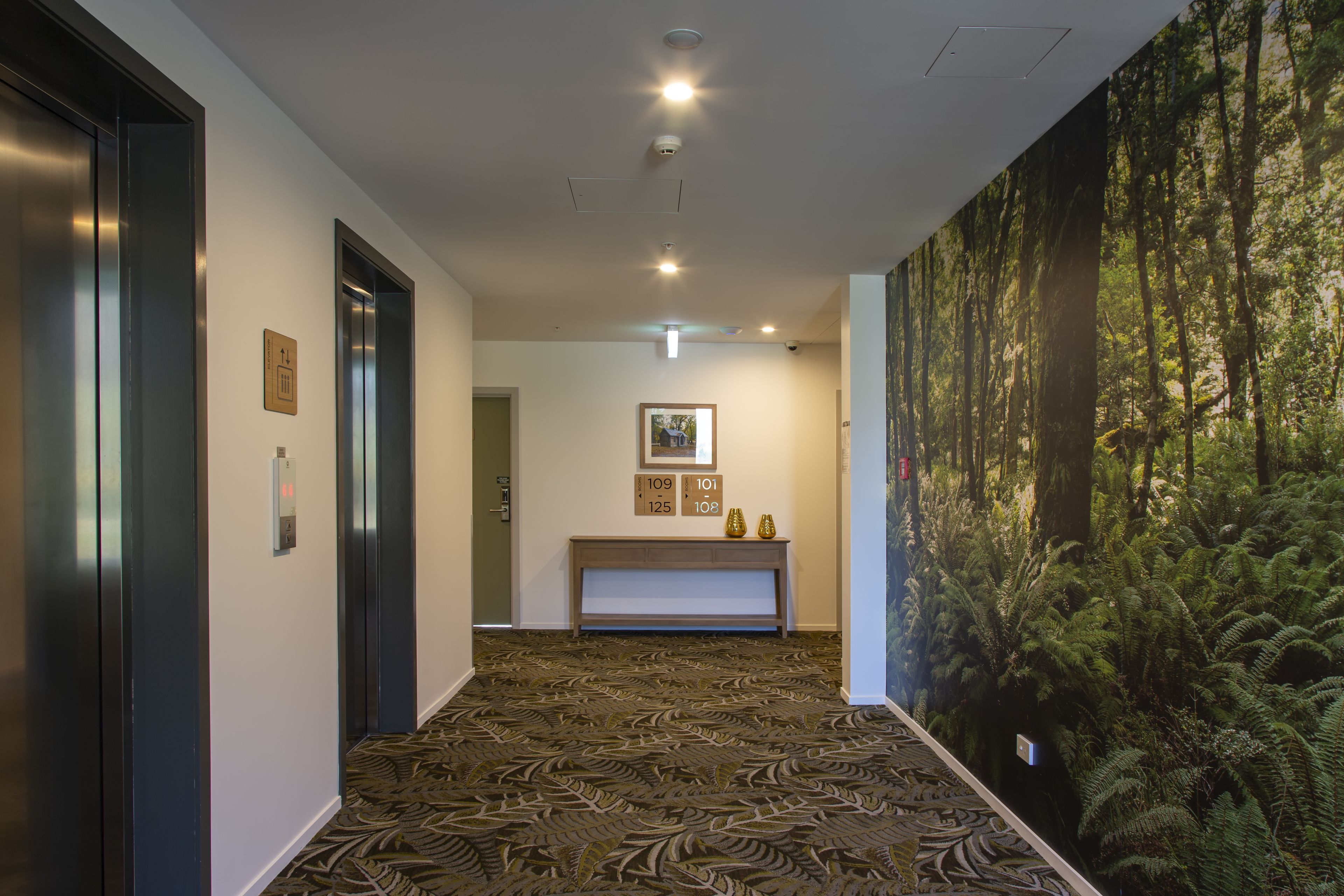 Un pasillo con alfombra estampada, una consola fijada a la pared y un mural con temática forestal.
