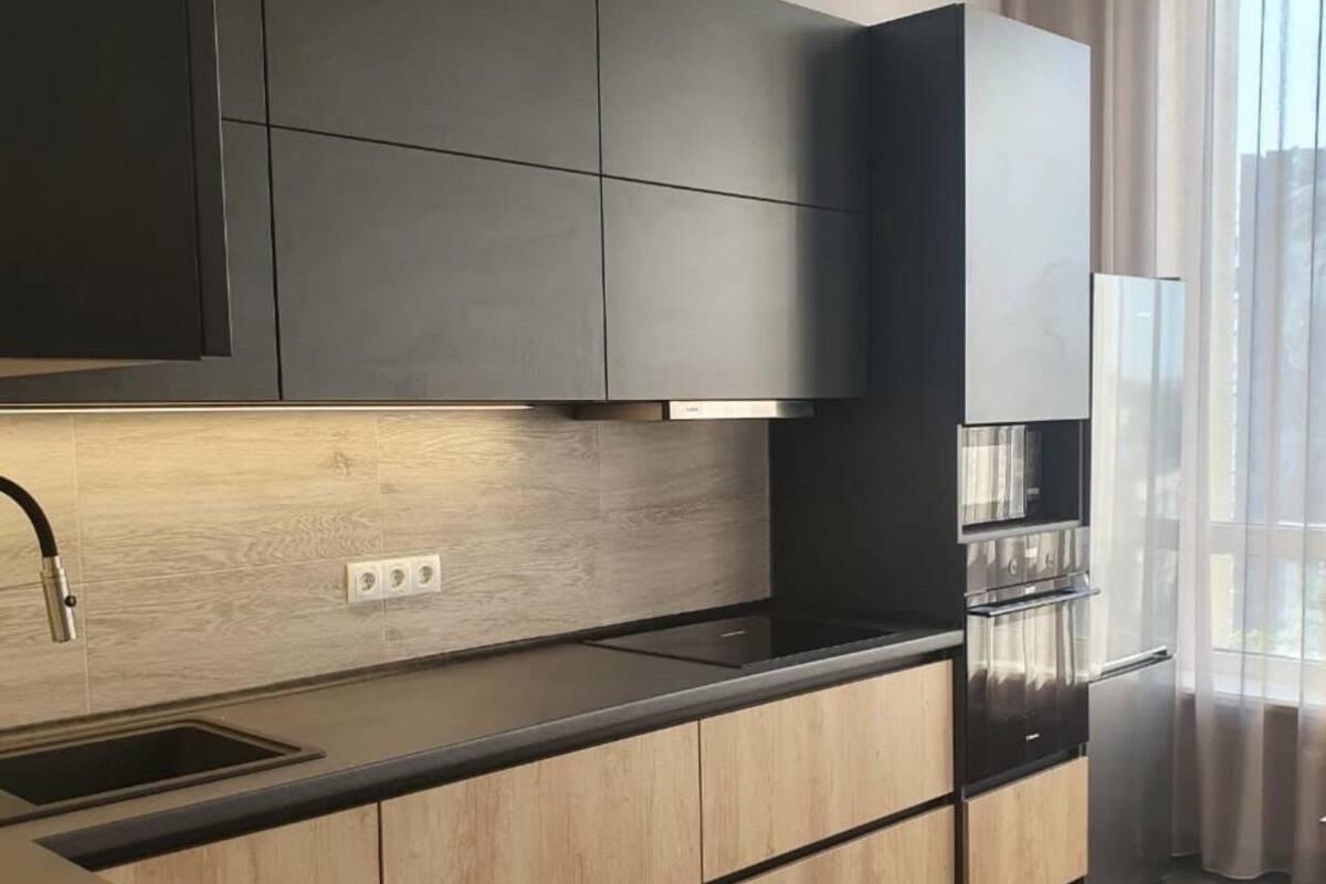 A modern kitchen with dark cabinets, a stainless steel range hood, and a built-in oven.