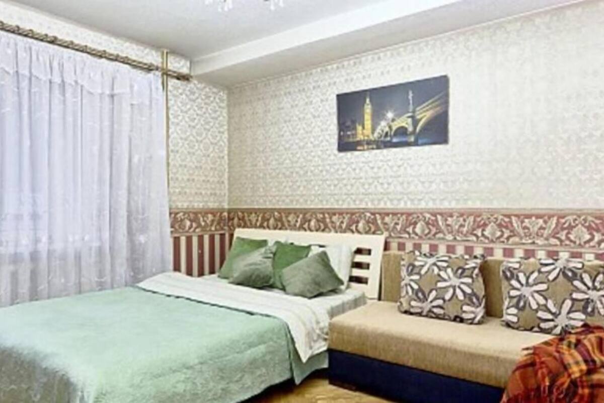 A bedroom with a bed, a sofa, patterned cushions, and a wall with a cityscape painting.