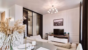 Uma sala de estar moderna com um sofá, uma mesa de centro de vidro, uma televisão e um candelabro.