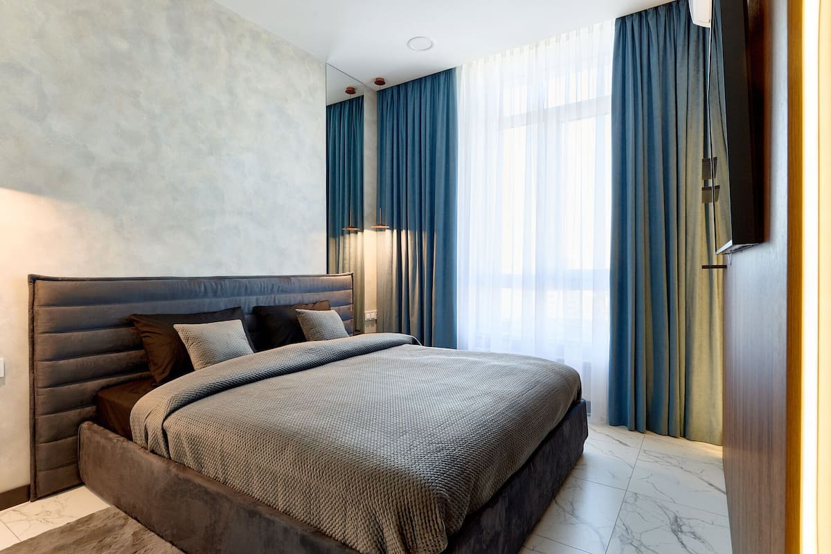 A modern bedroom with a large bed, dark headboard, and blue curtains.
