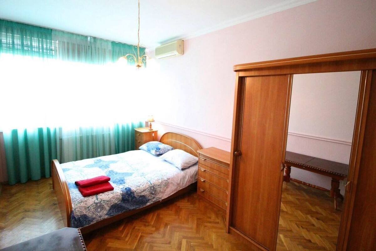 A bedroom with a bed, a wooden wardrobe, a bedside table, and a bench.