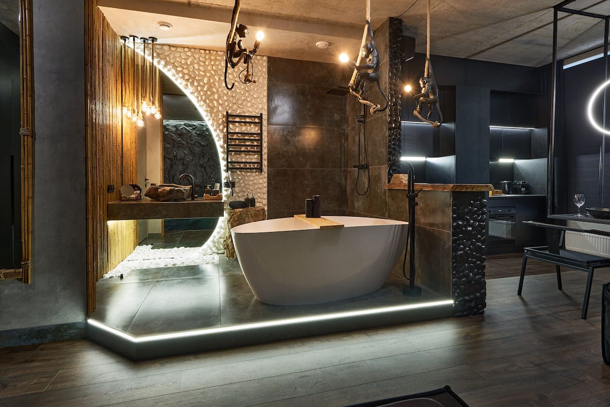A modern bathroom with a freestanding bathtub, a wooden vanity, and a stone accent wall.
