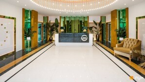 Uma área de recepção de hotel com design moderno, incluindo um balcão de atendimento, um espaço para sentar e um lustre decorativo no teto.