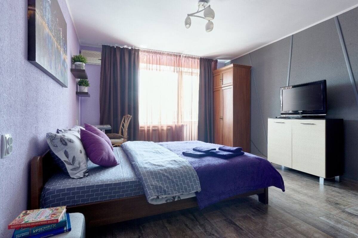 A bedroom with a bed, a TV, a wardrobe, and a window with curtains.
