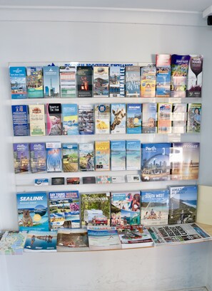 A wall of travel brochures and maps, including destinations like Swan River Cruises, Perth Zoo, and the Sunset Coast.