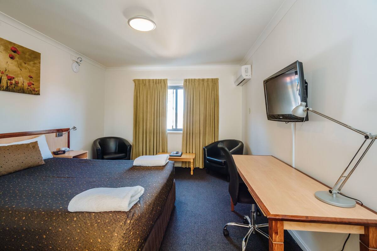 Ein Hotelzimmer mit Bett, Schreibtisch, Stuhl, Fernseher und einem fenster mit Vorhängen.