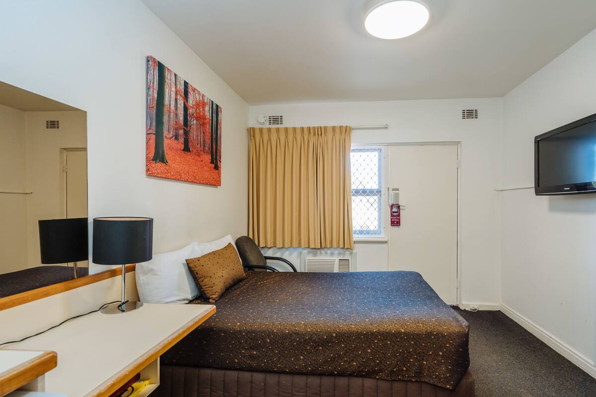 Ein Hotelzimmer mit einem Bett, einem Schreibtisch mit Lampe, einem Fernseher und einem Bild an der Wand.