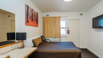 A hotel room with a bed, a desk with a lamp, a television, and a painting on the wall.