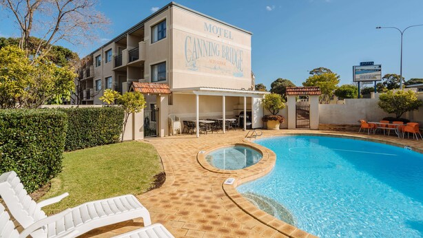 A motel with a swimming pool, outdoor seating, and a well-maintained lawn.