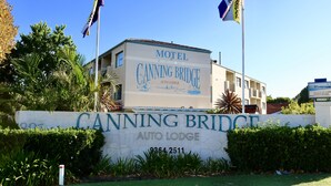 A motel named 'Canning Bridge Auto Lodge' with a large sign and two flags.