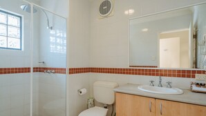 A bathroom with a glass-enclosed shower, a toilet, and a sink with a mirror above it.