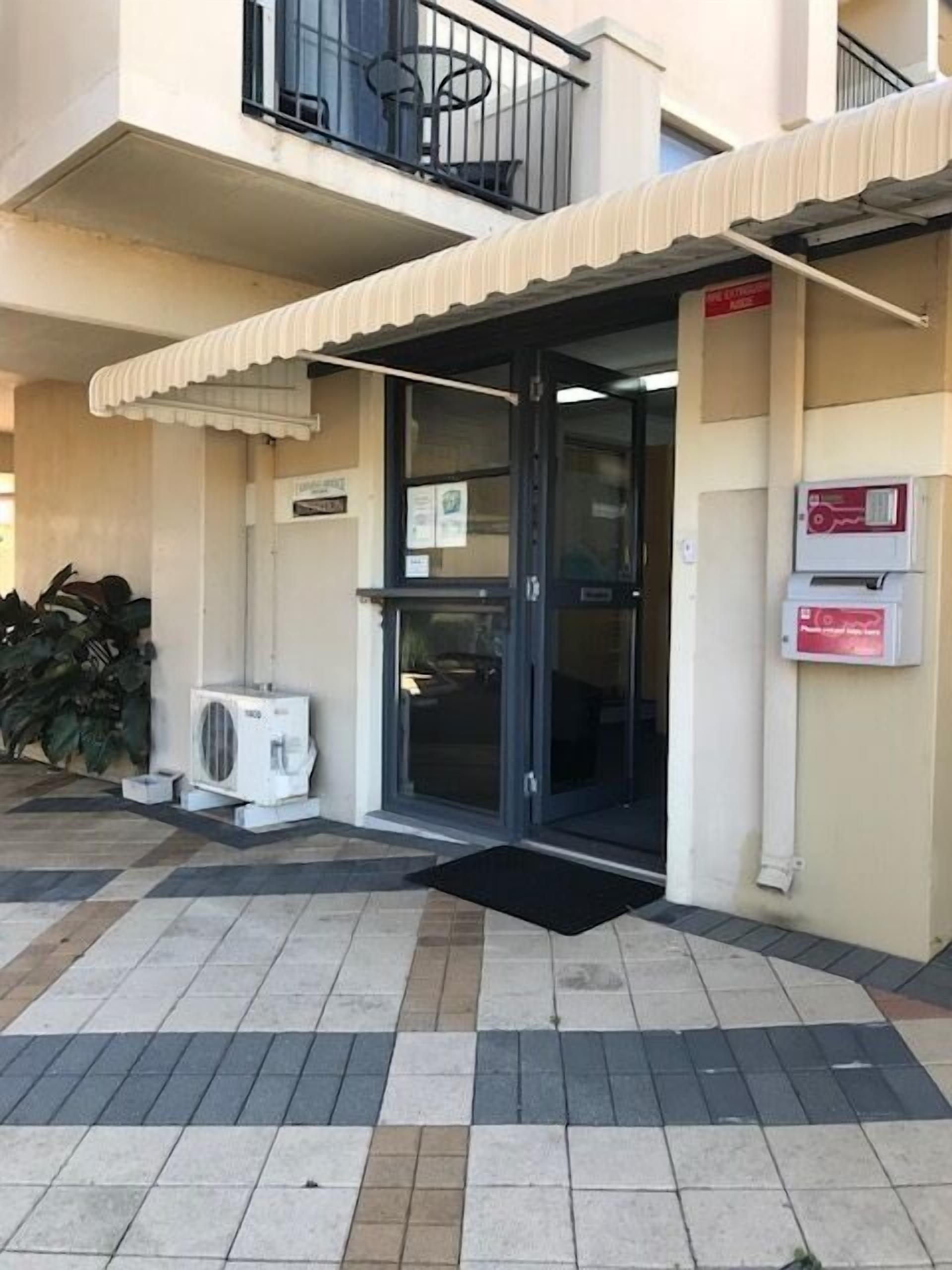 A building entrance with a tiled floor, a black door, and a small air conditioning unit outside.