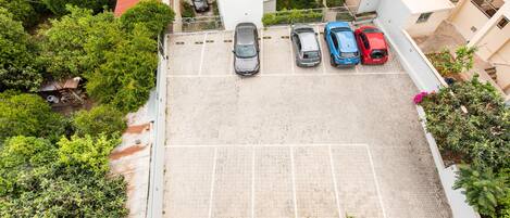 An aerial view of a parking lot with several cars parked, surrounded by greenery and buildings.