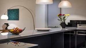 A modern kitchen with a central island, pendant lights, a bowl of fruit, and a vase with flowers. - Spring Apartments (Chania)