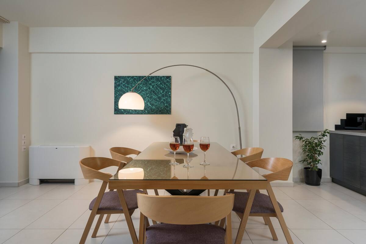 A modern dining area with a glass table, wooden chairs, and a pendant light.