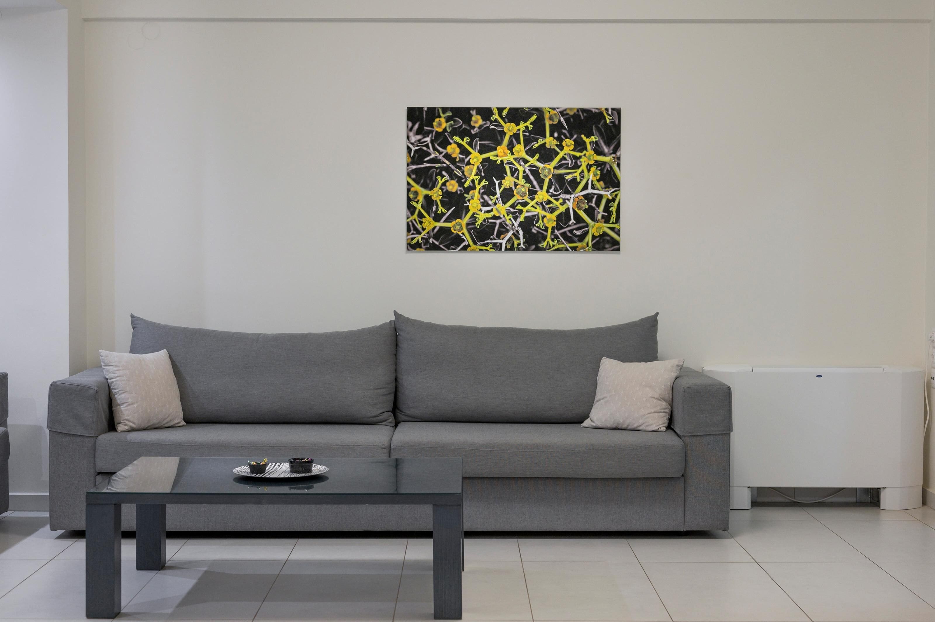 Un salon moderne avec un canapé gris, une table basse noire et un tableau abstrait noir et jaune accroché au mur.