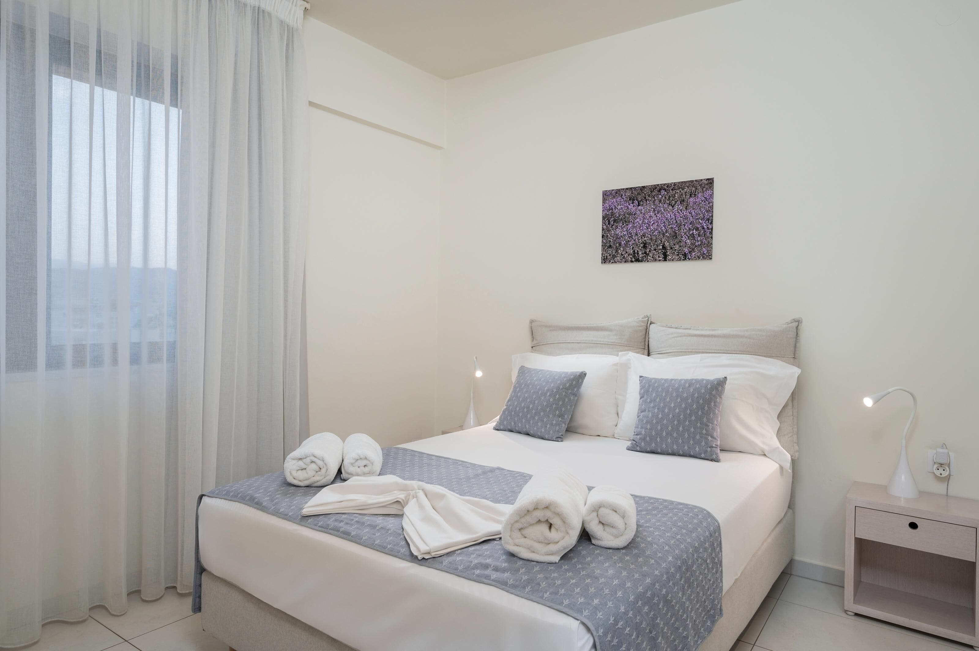 Una cama bien tendida con almohadas y toallas, una mesita de noche con lámpara y un cuadro en la pared.
