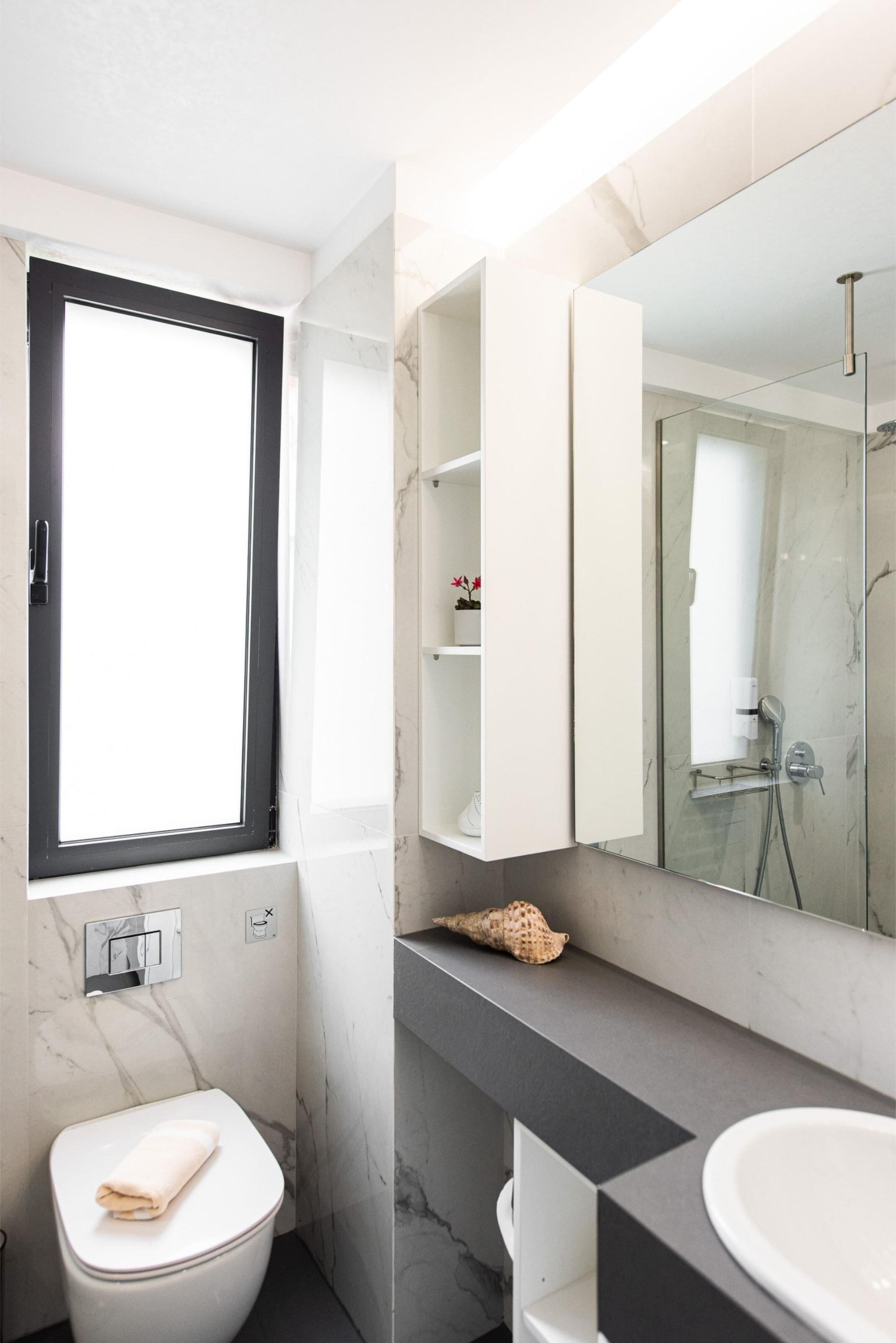 A modern bathroom with a toilet, a sink, a large mirror, and a shower.