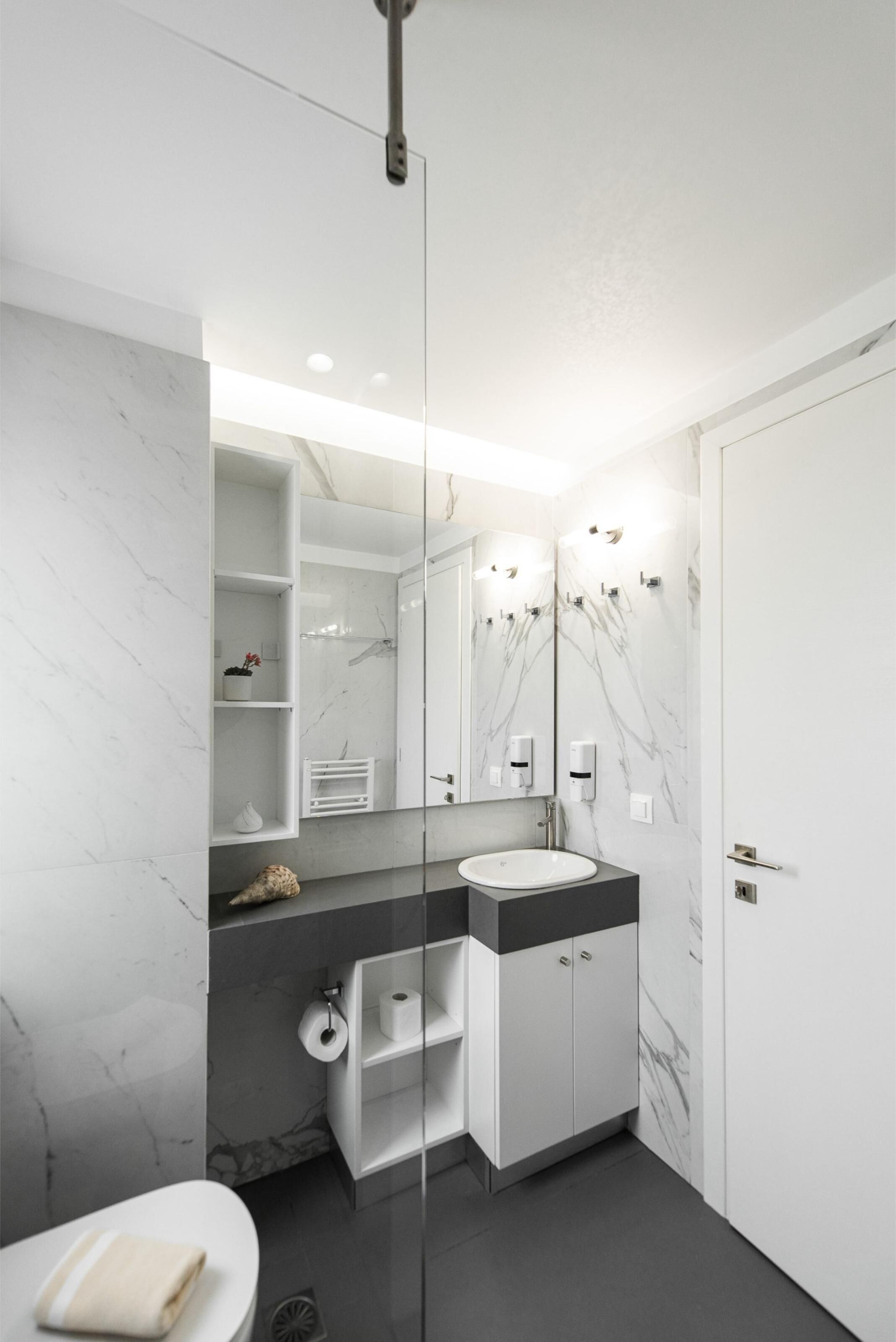 A modern bathroom with a marble vanity, a large mirror, and built-in shelves.