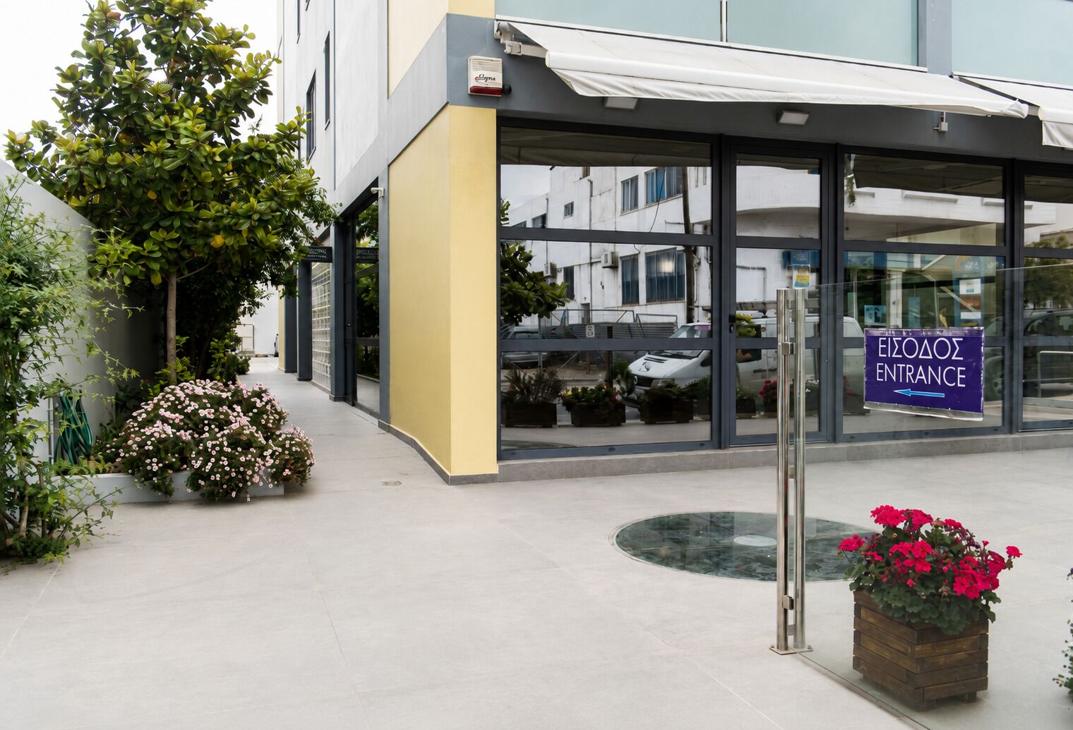 Un bâtiment doté d’une entrée en verre, d’une enseigne indiquant l’entrée et d’un bac à fleurs.