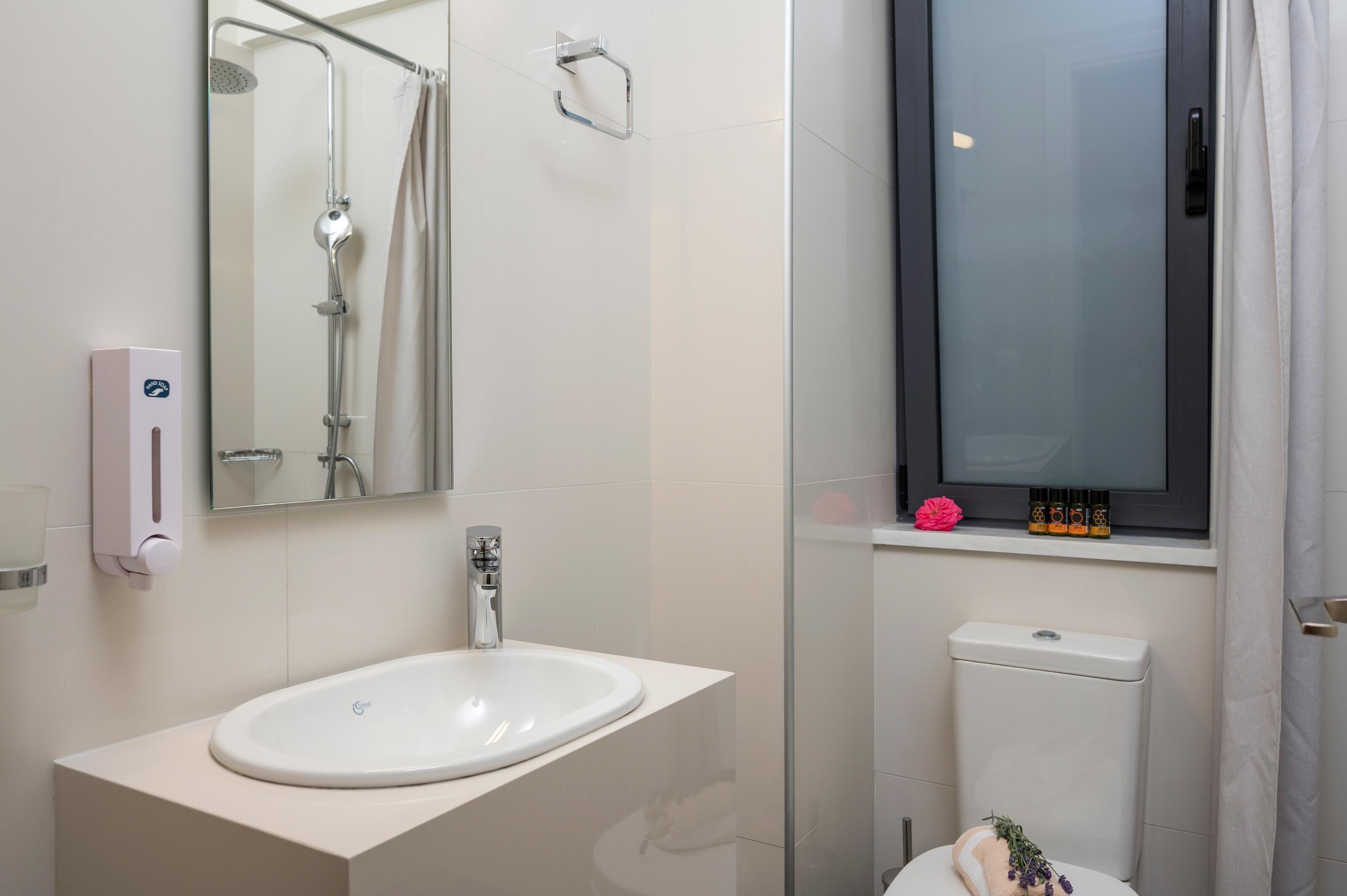 Een moderne badkamer met een witte wastafel, een douchecabine van glas, een toilet en een raam met gordijn.