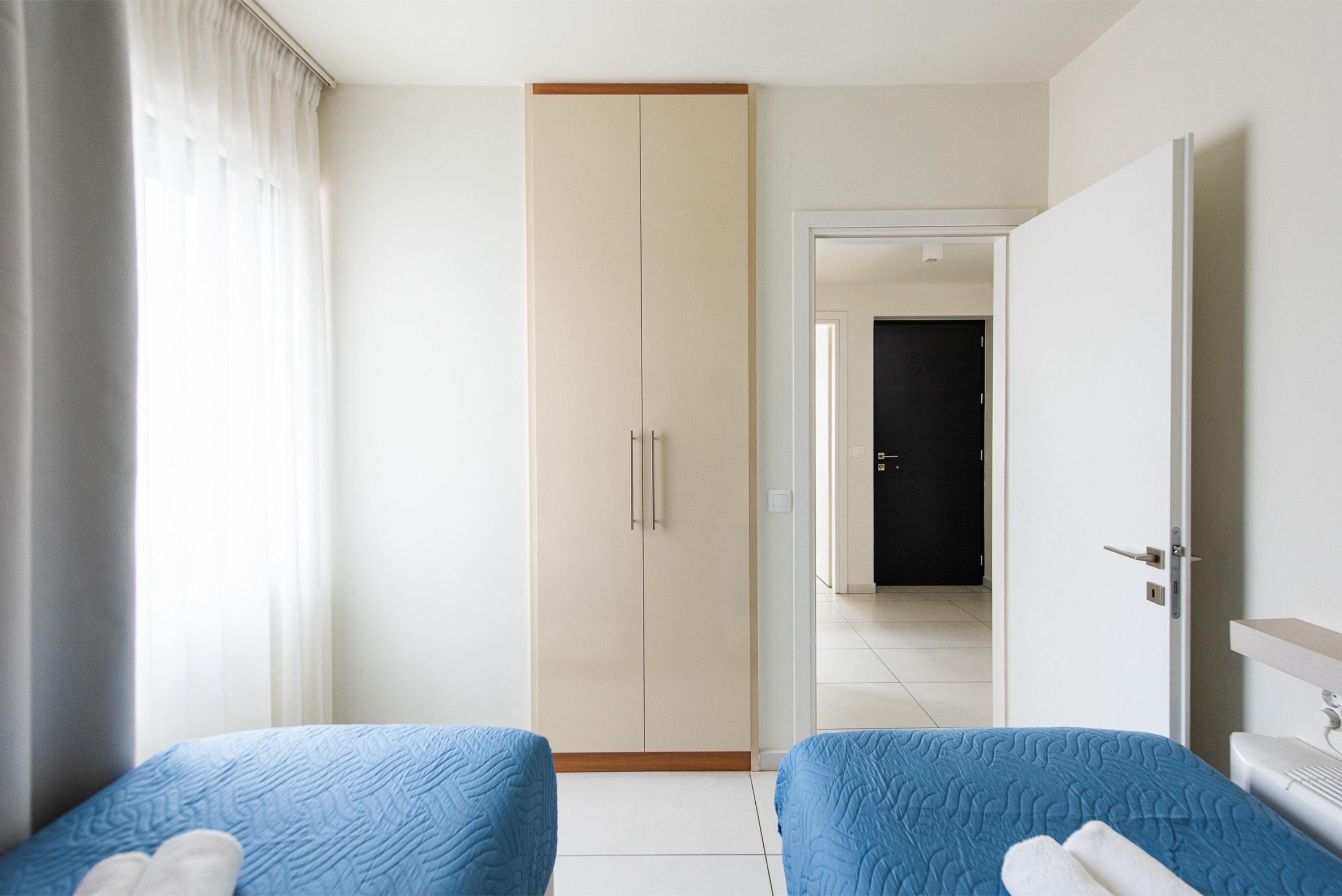Habitación de hotel con dos camas, un armario, baño y vista al pasillo.