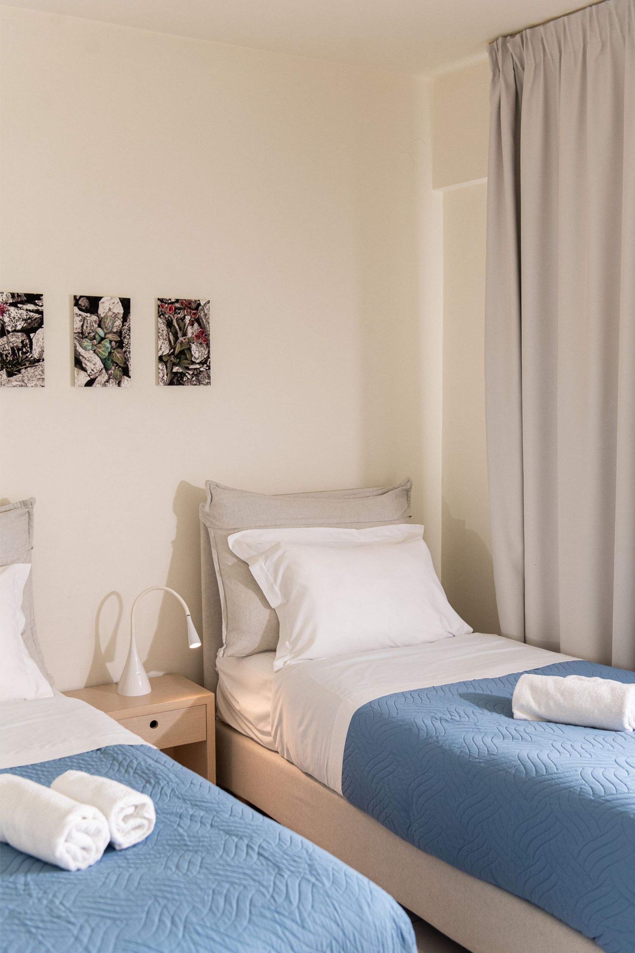 A hotel room with two beds, a nightstand, a lamp, and three framed pictures on the wall.